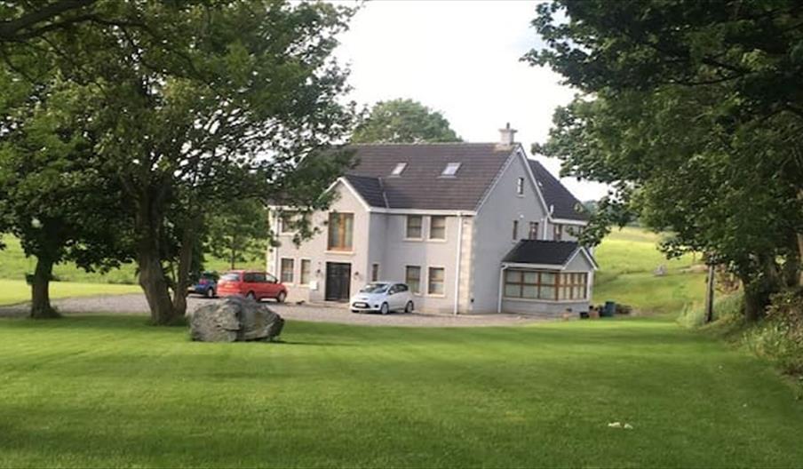 View of outside of the property, surrounded by mature trees and two cars parked on the driveway