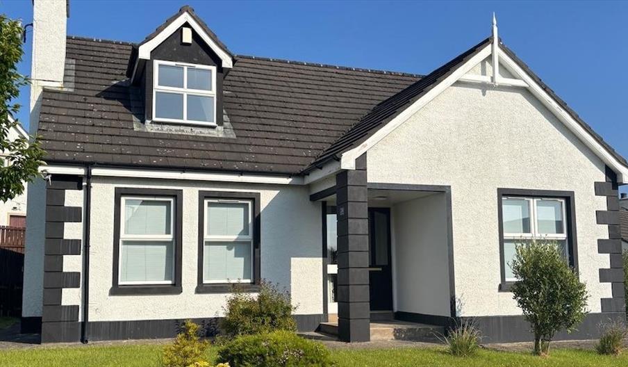 Front view of house with white rendered walls, dark grey trim and a pitched roof with a dormer window