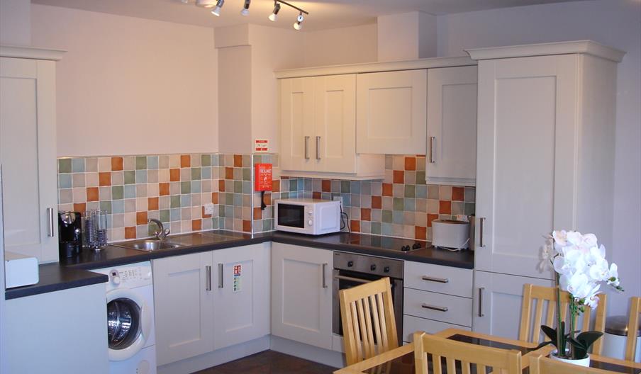 Kitchen with cream cabinets, multi-coloured tile backsplash, and a small wooden dining table with chairs.
