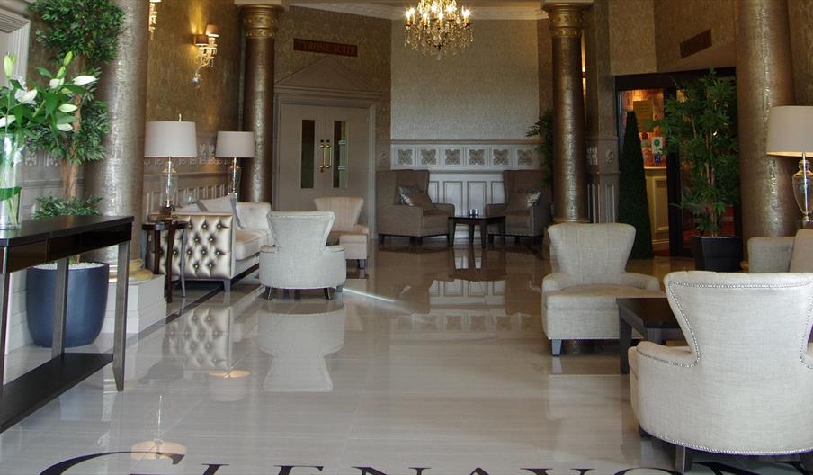 Image of the entrance hall with shiny tiled floors, cream armchairs, gold metallic columns and patterned wallpaper