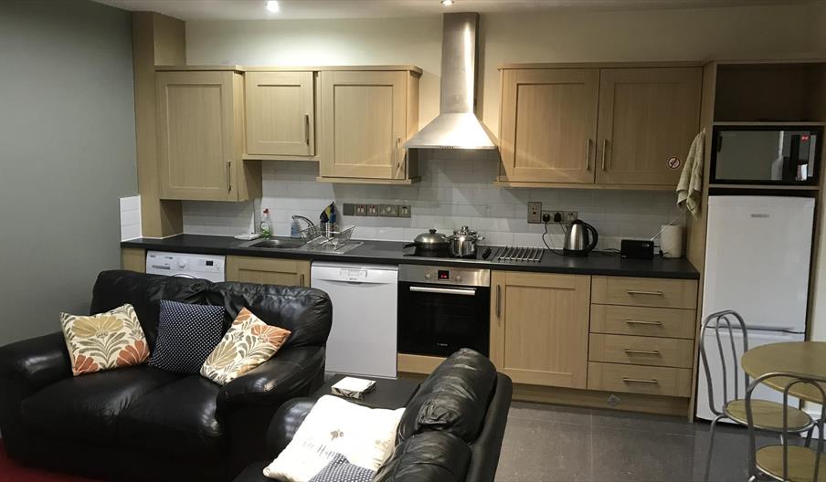 An open plan, kitchen and sitting room with black sofas.