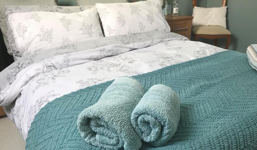 Image shows double bed with rolled up towels at the bottom