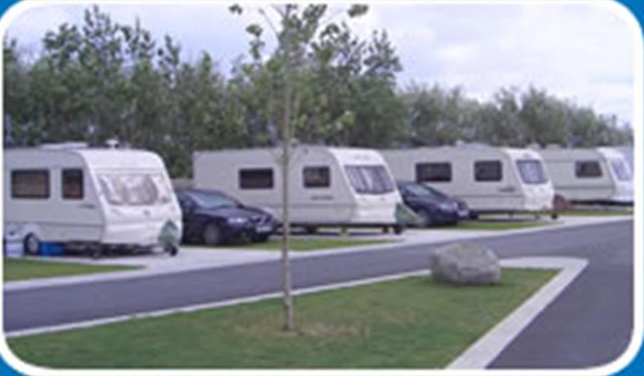 A road in a caravan park with 4 caravans and parked cars.