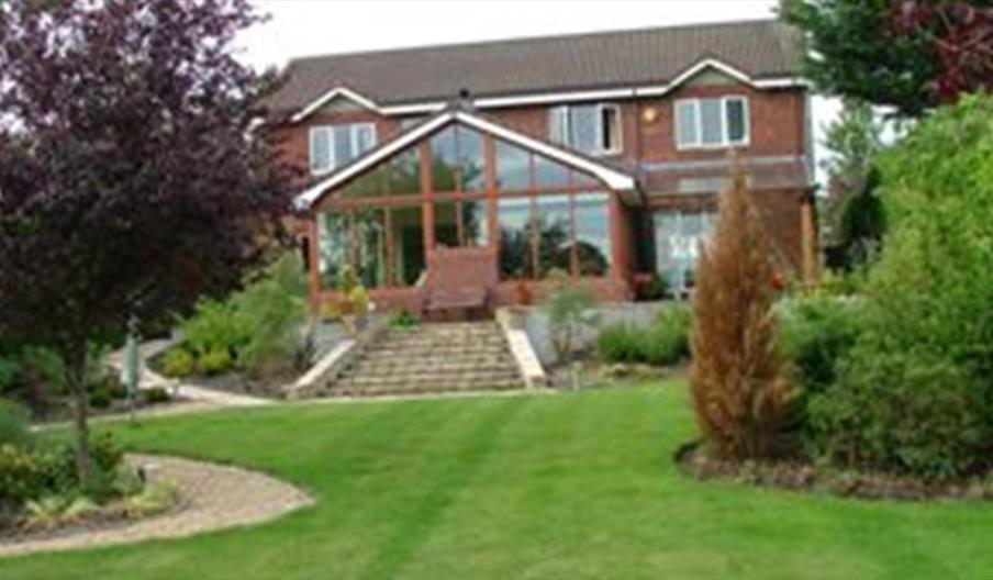 A large B&B on a lawn with trees and stone stairs leading to a large conservatory.