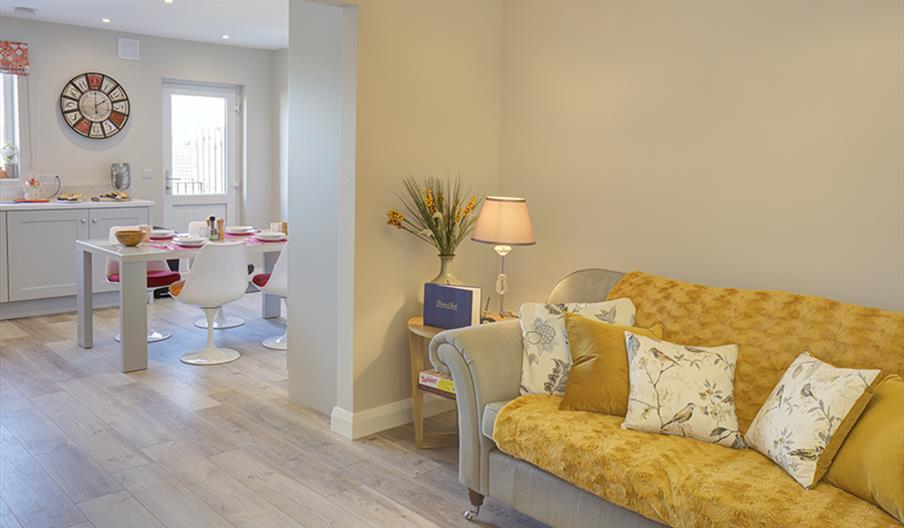 Open plan lounge area with a yellow sofa leading into a kitchen/dining room.