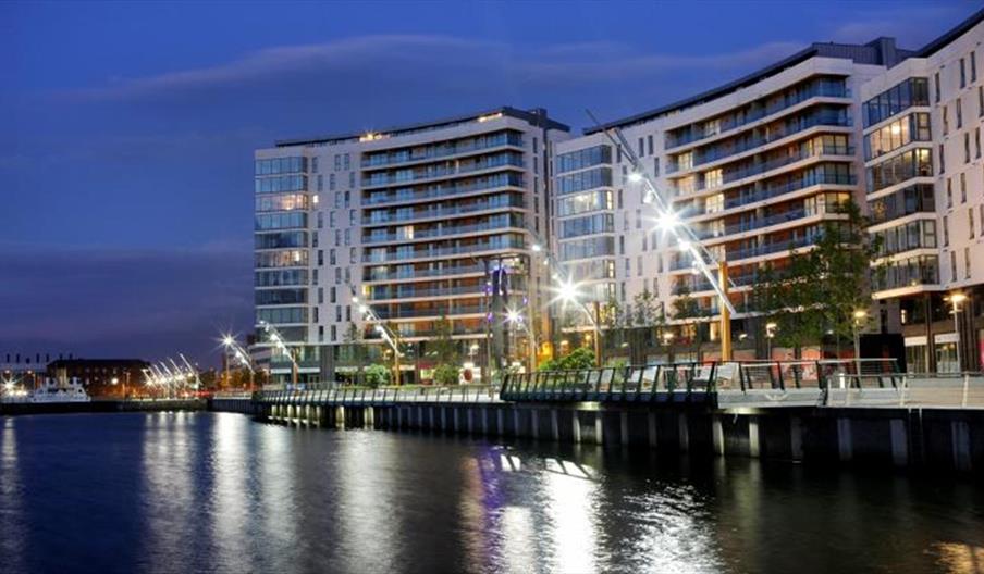 A curving apartment building at night on a seaside walkway.