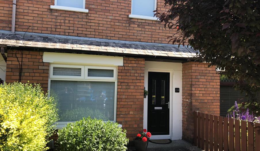 A photo of the front of a house with a black front door and bushes in the garden.