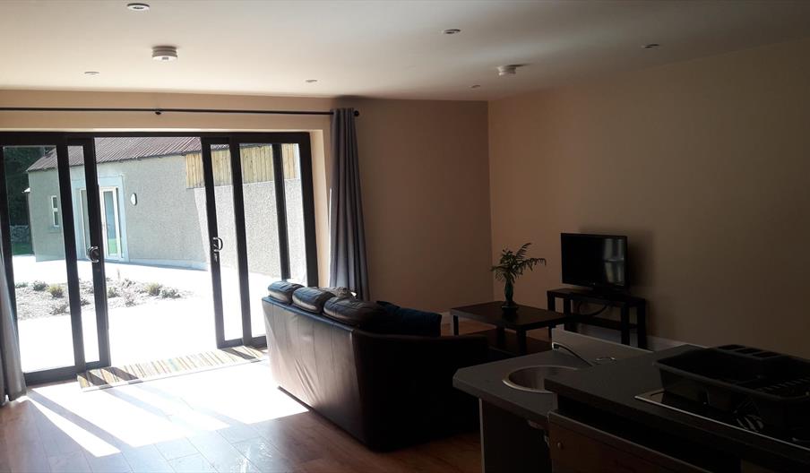 Living area with a sofa facing a small TV and large glass doors opening to an outdoor patio.
