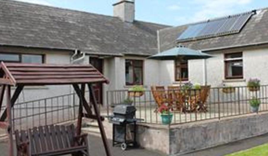 Outside image of house with accessibility ramp, table and chairs, wooden swing chair