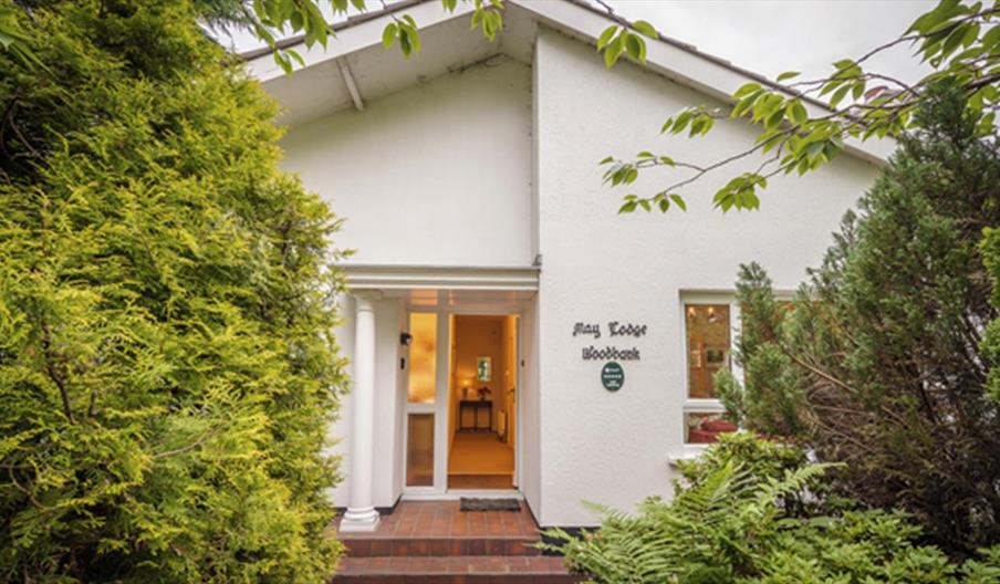 Front door of lodge decorated with large bushes and trees.