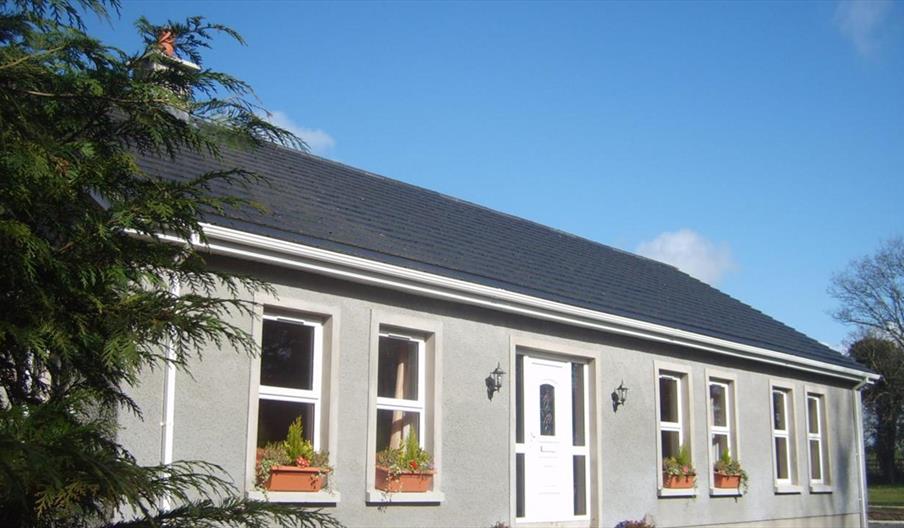 A single-story lodge with a tree and plant pots on the window ledges.