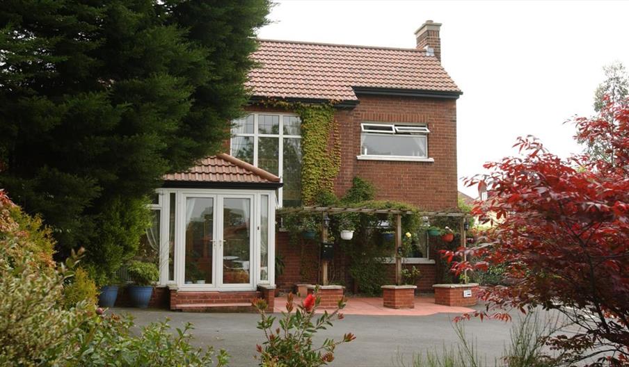 A B&B seen through a colourful garden of trees, bushes and flowers.