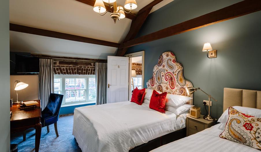 Image shows bedroom with one double bed and one single bed with low window and door to ensuite open