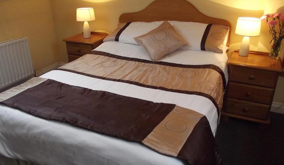 A double bedroom with a brown throw and pillows and nightstands with lamps and flowers.