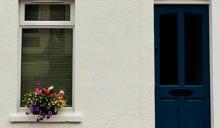 The front of a house with a dark blue door and a window decorated with flowers.