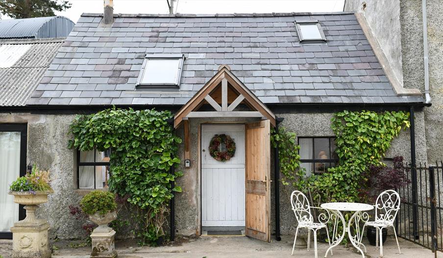 Outside view of Milk House with greenery on the walls and outside table and 2 chairs