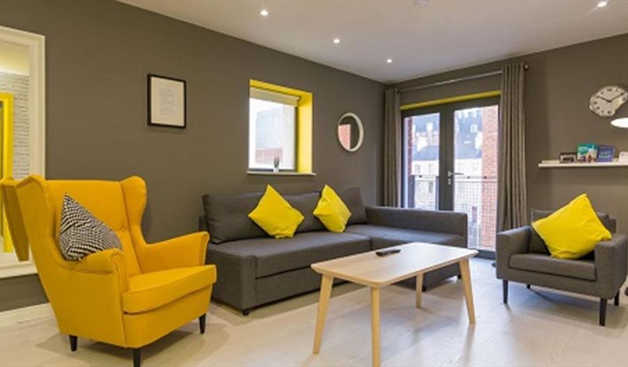 A grey sitting room with grey and yellow chairs, a grey sofa and a coffee table.