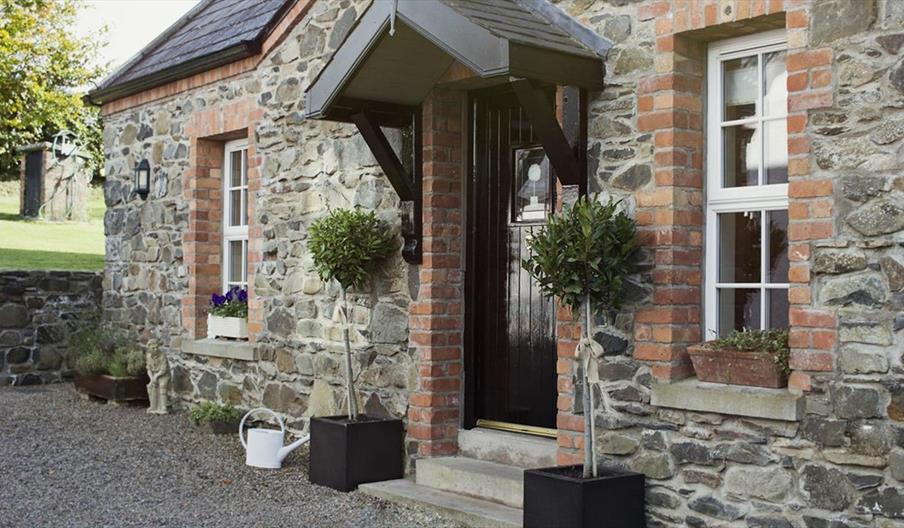 Image shows outside of stone property with bay tree plants at either side of front door