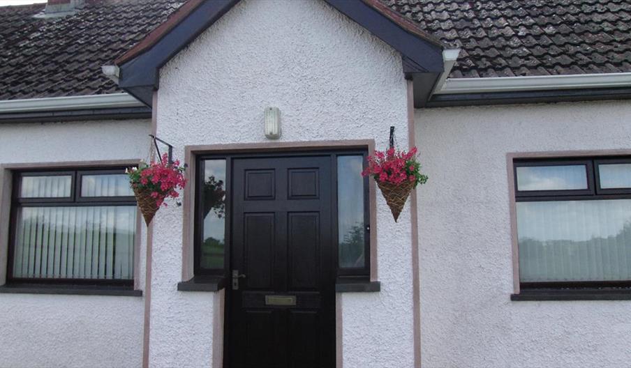 Image of the front of a white bungalow with flower baskets hanging on either side of the door