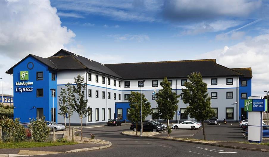 A large blue three floor hotel with a car park.