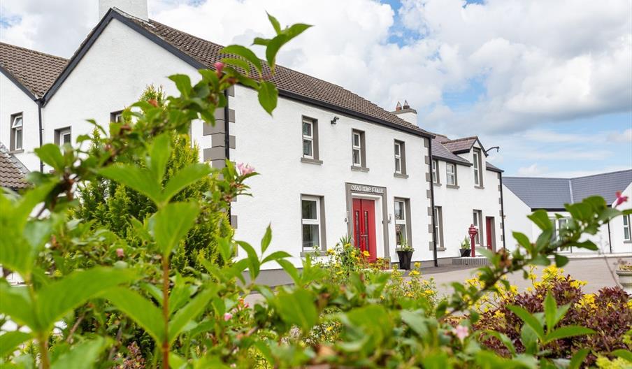 Exterior view of Willow House, a white Edwardian manor with a red front door and lush green garden foreground.