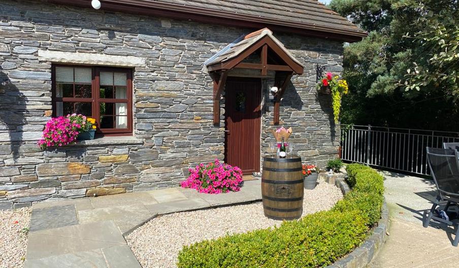 Front garden with paved path leading to the cottage's front door, decorated with flowers and a barrel.