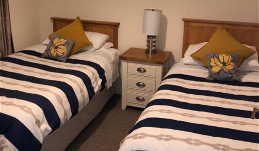 Image shows twin bedroom with bedside table and lamp between the beds
