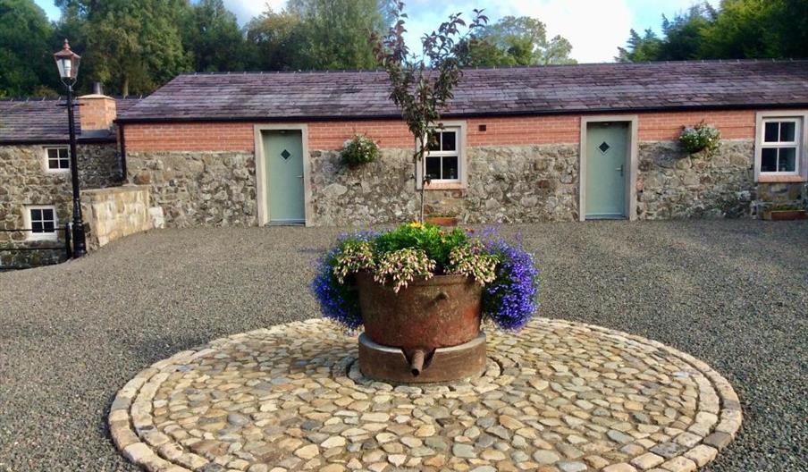 Image shows front of cottages with flower bed in a stone circle