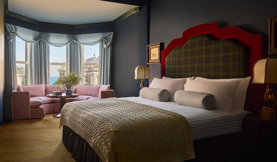interior of double bedroom at Adelphi Hotel - features a tartan headboard and knitted throw on the bed, as well as a low pink sofa by the window overl