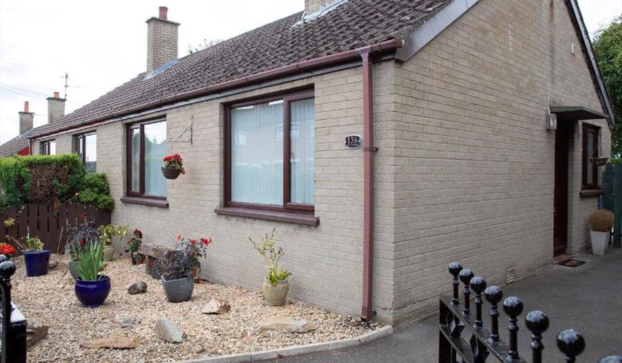 An Image of the front of the semi-detached bungalow with driveway to the side and set of gates.
