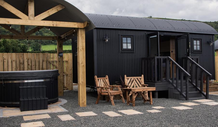 Hot tub beside a black Shepherds Hut with step entrance and seats outside at Shepherds Rest Luxury Glamping in Carnlough