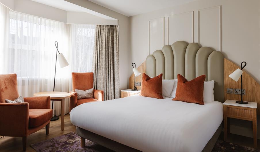 Contemporary hotel bedroom with king-size bed, statement headboard, seating area and soft neutral décor.