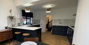 Large kitchen with worktop stools and a doorway leading to a staircase.