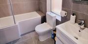 Tiled bathroom with bath/shower, toilet and a sink with a mirror.