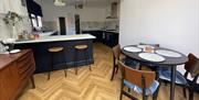 Dining area with table and chairs and worktop stools leading into a kitchen.