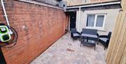Paved outdoor seating area with garden furniture and an electric car charger on the wall.