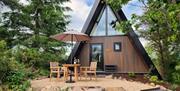 A five-star A-frame lodge set among trees, with an outdoor dining area and parasol on a private patio surrounded by landscaped gardens.