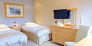 A twin bedroom with two single beds, a chair, a chest of drawers and a TV.