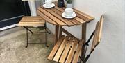 A small garden table set against a wall in a small entry with coffee cups.