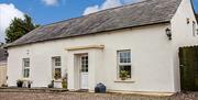 Image shows front of cream painted cottage with flowerbeds on windows and gravel drive
