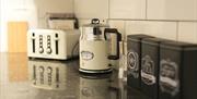 A kitchen countertop with a toaster, kettle, tea, coffee and sugar.