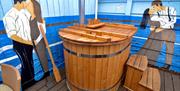 A photo of a wooden hot tub sitting on a deck, surrounded by murals of Titanic couples embracing on the walls.