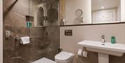 Modern hotel bathroom with walk-in rainfall shower, illuminated mirror, sink and contemporary marble-effect finishes.