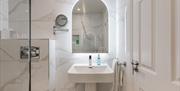 Bright contemporary bathroom featuring a walk-in shower, illuminated mirror, pedestal sink and marble-effect tiling.