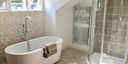 Image shows stand alone bath with tall radiator and shower cubical. Small window above bath