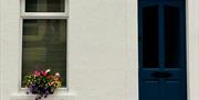 The front of a house with a dark blue door and a window decorated with flowers.