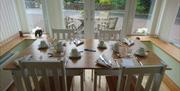 Table set for breakfast with four chairs, two either side. Patio doors behind the table which looks out over the garden with a wooden table and chairs
