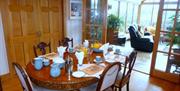 A fully set dining room table in a dining room with doors leading to a large conservatory.