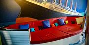 A photo of a boat-shaped couch with red cushions set against a mural of the Titanic, in a themed apartment.
