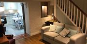Image shows lounge area with sofa under the stairs, wooden floor and door way into kitchen open